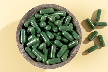 Green spirulina capsules on yellow background. Natural supplement for detox, energy. Top view.