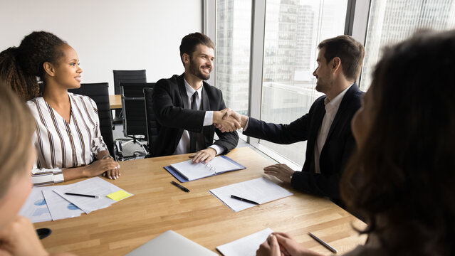 Smiling boss shake hand of millennial worker on staff meeting