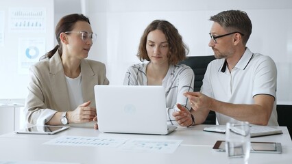 Professional team reviewing project data on laptop, working together in modern office environment, collaborating with focused corporate energy. Business people concept