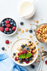 Yogurt with fresh berries and granola on white table.