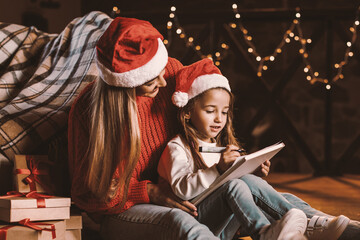 Wishlist. Little girl wearing red hat writing letter to Santa, asking for presents under tree on...