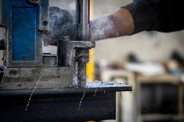 Worker using a magnetic drill press on a steel beam in a workshop.