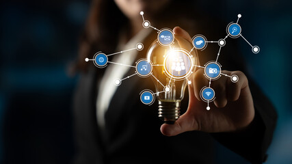 A businesswoman holds a light bulb surrounded by digital connectivity icons, representing innovation and modern technology in the business landscape. Tessel