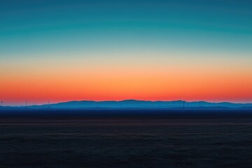 Fototapeta premium Vibrant gradient sunset above a wind farm, with layered blue mountains and a dark field, symbolizing renewable energy and serene landscape.