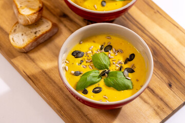 Delicious pumpkin soup served in red bowls, garnished with fresh basil leaves, sunflower and pumpkin seeds