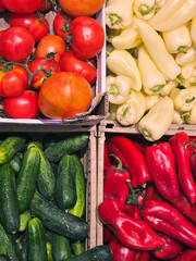 Fresh vegetables at a market stall: ripe tomatoes, cucumbers, red peppers, and pale yellow peppers. Vibrant colors showcasing healthy, natural produce.