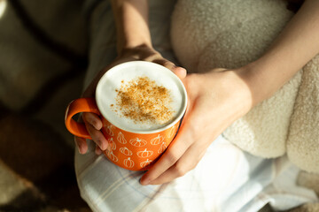 Close-up of a person holding a cozy autumn drink in an orange mug decorated with pumpkin illustrations, pumpkin latte in cute mug with cinnamon, autumn vibe 