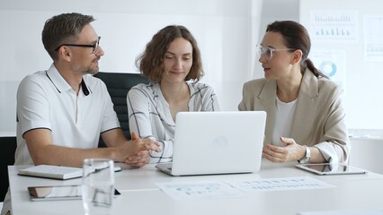 Professional team reviewing project data on laptop, working together in modern office environment, collaborating with focused corporate energy. Business people concept