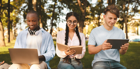 International college classmates preparing for lectures outdoors, sitting in university campus with books, laptop and tablet. Break between classes concept
