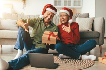 Online Christmas. Happy Senior Couple Video Calling Using Laptop Celebrating Xmas Holiday Holding Wrapped Gift Box At Home. New Year Season, Modern Distance Communication