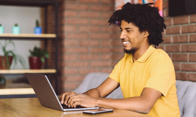 Modern Career. Cheerful Black Freelancer Guy Working Online With Laptop At Table In Cafe, Smiling Young African American Man Typing On Computer, Enjoying Remote Work Opportunities, Copy Space