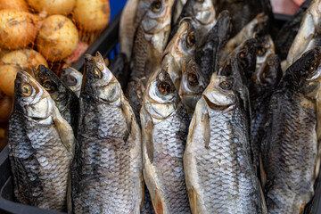 Dried fish displayed for sale with onions in the background.