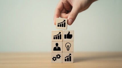 Hand placing a wooden block with a rising bar graph icon on top of other blocks with various business icons. A symbol of growth and progress