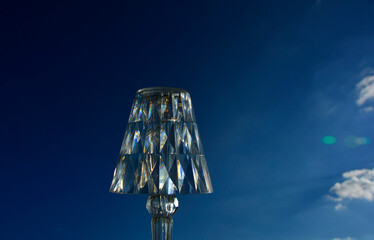lampka z pleksi na tle nieba, dekoracyjna lampka stołowa oświetlona słońcem na tle nieba, decorative table lamp illuminated by the sun against the sky,