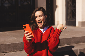 Happy brunette long hair business student woman sitting on stairs outside using mobile phone...