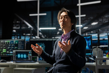 Computer scientist in server room using device to review infrastructure diagnostics. Asian senior programmer in high tech data center analyzing performance data to maintain system uptime