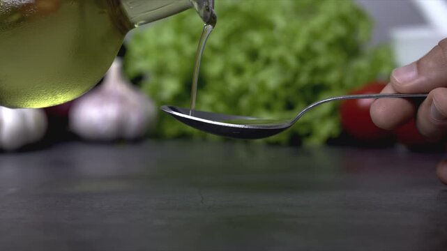 Pouring Olive Oil from Bottle onto Tablespoon with Fresh Vegetables in Background
