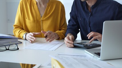 Professional accountants working in a well lit office, analyzing financial data and reviewing statements with a calculator and pen. Audit and taxes theme in business