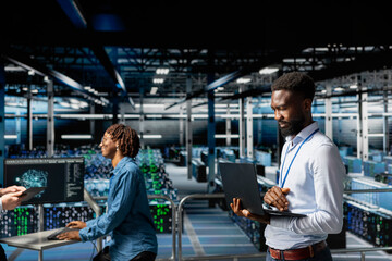 African american smiling engineer in data center monitoring neural network LLM visualization, Server hub IT specialist overseeing machine learning processes for infrastructure development.