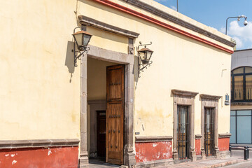 A building with a yellow facade and red trim. The front door is open. Historic center of Queretaro, colonial architecture, decorations for the celebration of Mexico's Independence Day.