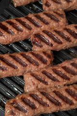 Grilled minced meat sausages, barbecue concept, culinary application, outdoor cooking context — close-up of juicy meat rolls with seared grill marks sizzling on a barbecue pan, showing texture and fla