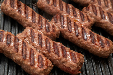 Grilled minced meat sausages, barbecue concept, culinary application, outdoor cooking context — close-up of juicy meat rolls with seared grill marks sizzling on a barbecue pan, showing texture and fla