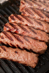 Grilled Chevapchichi (Cevapi) on a Black Cast Iron Griddle, Close-up of Sizzling Meat Kebabs with Grill Marks, Balkan Cuisine BBQ Food, Overhead Macro Stock Image