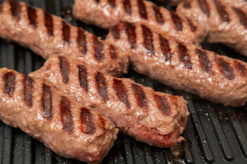 Close-up of traditional grilled minced meat rolls (Mici or Cevapcici) cooking on a hot grill pan, showing rich grill marks and sizzling texture, perfect for food, cooking, Eastern European cuisine, an