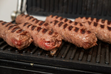 Grilled Chevapchichi (Cevapi) on a Black Cast Iron Griddle, Close-up of Sizzling Meat Kebabs with Grill Marks, Balkan Cuisine BBQ Food, Overhead Macro Stock Image