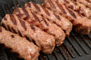 Grilled minced meat sausages, barbecue concept, culinary application, outdoor cooking context - close-up of juicy meat rolls with seared grill marks sizzling on a barbecue pan, showing texture and fla