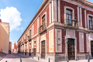 A row of buildings with balconies and a red and white building. The buildings are old. Historic center of Queretaro, colonial architecture, decorations for the celebration of Mexico's Independence Day