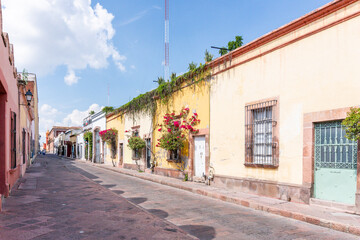 A street with a lot of buildings and a few people walking around. The buildings are yellow. Historic center of Queretaro, colonial architecture, decorations for the celebration of Mexico's Independenc