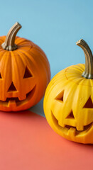 Two carved pumpkins, orange and yellow, sit on coral and blue background, showcasing Halloween spirit and festive mood Free space for text