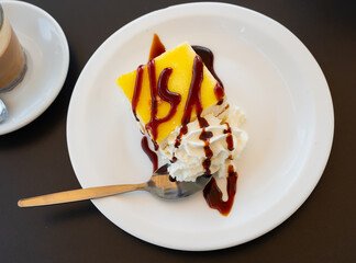 Slice of lemon biscuit cheesecake piece of delicate vanilla dessert with cream decorated with chocolate topping on plate