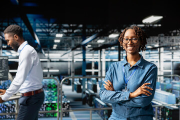 Happy IT expert in server hub reviews AI diagnostics on industrial platform, monitoring machine learning development. African american woman maintaining operational reliability, checkup.