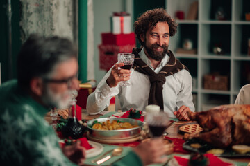 Happy man raising wine glass at christmas dinner with family