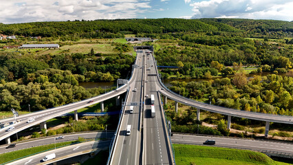 Aerial view of highway interchange with elevated ramps and cars, green countryside hills and...
