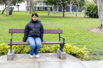 A teenager sits on a park bench in a park