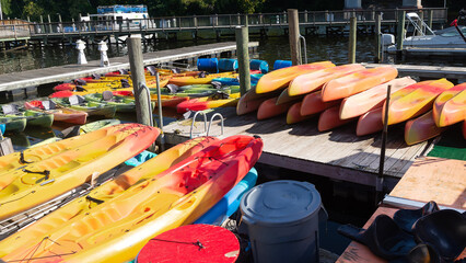 Stacked and floating kayaks at a waterfront rental pier under sunshine