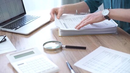 Close-up of man hands reviewing financial documents with magnifying glass. Business work process in...