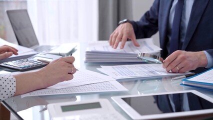 Business people wearing blue suits are reviewing financial data in office. Male auditor is using a magnifying glass. Audit and taxes concept