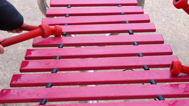 Musician playing red xylophone in playground. Vibrant red xylophone resonating melodic sounds while musician striking wooden keys with matching red mallets during playful outdoor performance