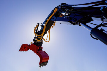 Modern crane arm with open grapple, industrial gripper on blue sky background