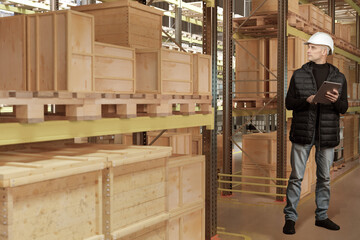 Worker in hard hat with tablet checking wooden crates on shelves in warehouse, concept of storage, logistics, inventory. Activity: Warehouse, logistics.