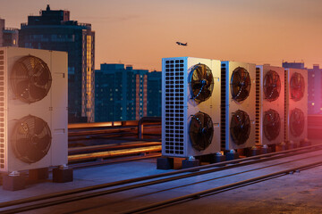 Air conditioning units on a rooftop with city buildings at sunset, airplane in sky, concept of...