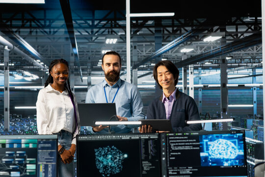 Portrait of smiling multiethnic engineers in data center troubleshooting server connectivity issues using AI. Upbeat multiracial technicians in diverse server room auditing systems for vulnerabilities