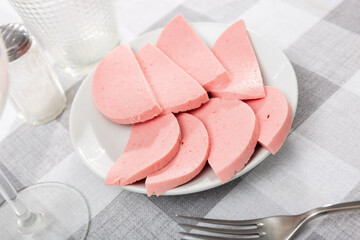 There are thick slices of boiled sausage on small round plate. Dinner preparation, appetizer and cutlery are served