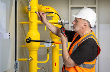 Worker in helmet and safety vest checking gas pipeline with detector, industrial inspection, safety...