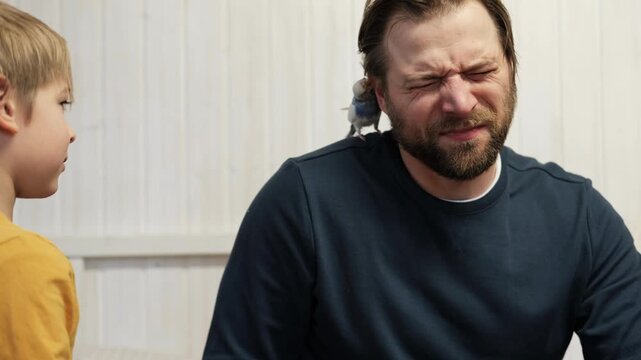 Father and son enjoying at home. Young boy and his daddy playing with funny pet budgerigar parrot. Happy family. Tamed budgie parakeet. People take care of and play with bird. Cute domestic animals