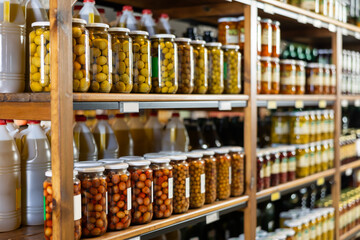 Glass jars with various pickled olives in brine displayed on shelves in grocery store, ready for customers to purchase. Organic artisanal produce